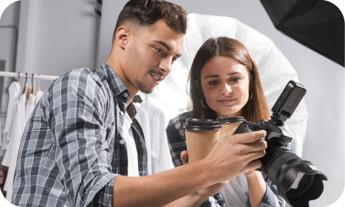 Dos jóvenes estudiantes revisando una cámara profesional en un estudio fotográfico, colaborando en una sesión de contenido visual.